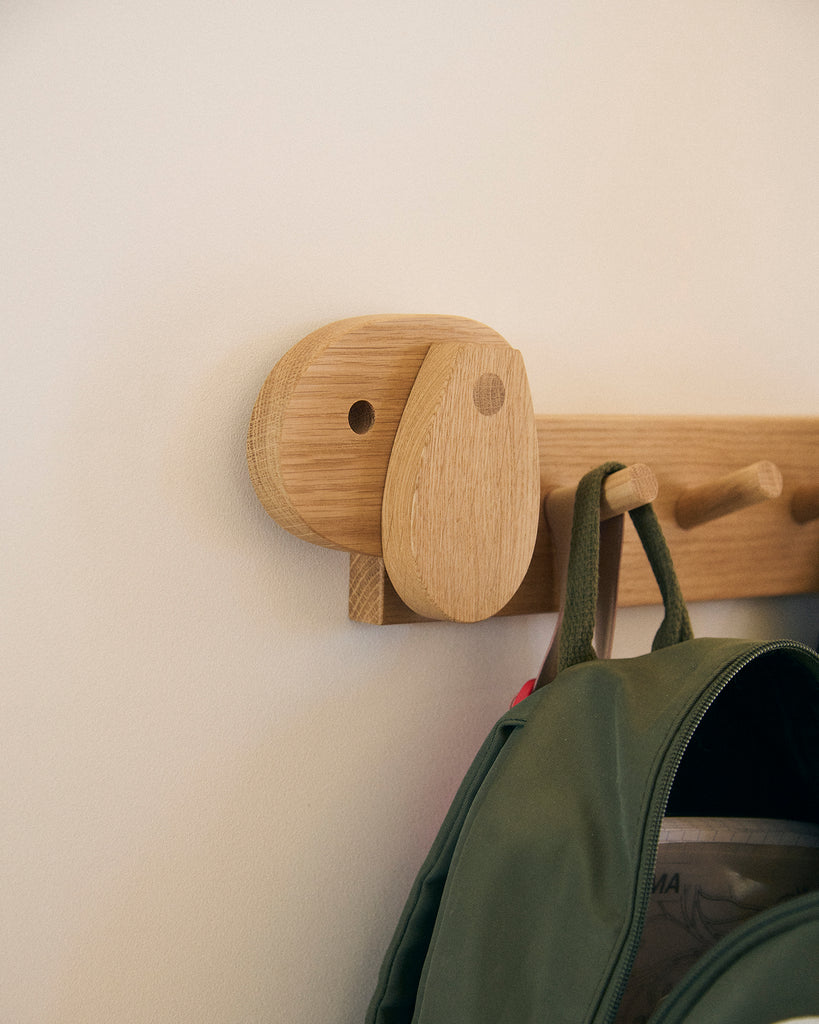 A wooden coat rack shaped like a dog with a green backpack hanging on a white wall.