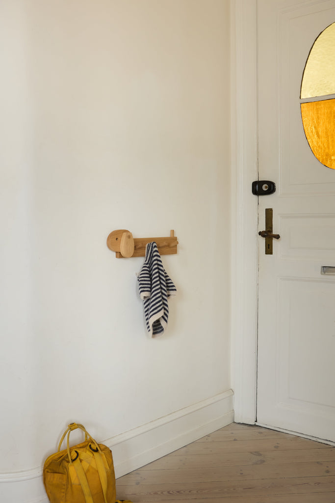 A wooden coat rack shaped like a dog with a striped shirt hanging in a hallway next to a white door.