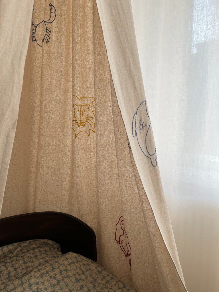 Sand colored bed canopy with handwoven zodiac signs hanging over a bed